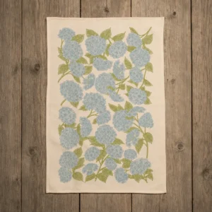 Full blue hydrangea cotton kitchen towel laid flat on a weathered wooden table.