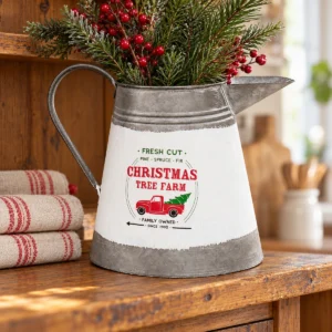 Christmas Tree Farm metal pitcher filled with pine greenery and red berries on a rustic entry table beside a Santa figurine.